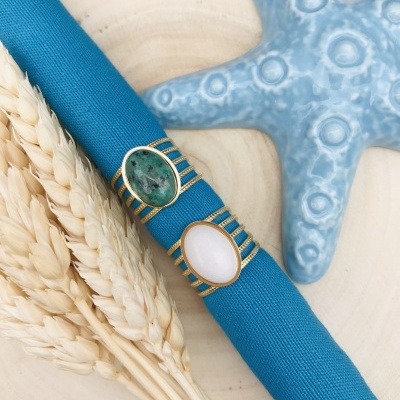 Anéis dourados com pedras em tecido azul junto a estrela-do-mar cerâmica e trigo seco