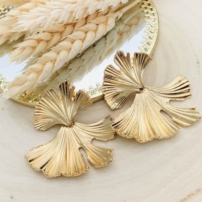 Brincos dourados em forma de folhas sobre madeira clara junto a espelho e ramos secos