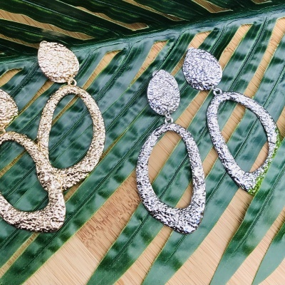 Dois pares de brincos texturizados, dourado e prateado, sobre folhas verdes