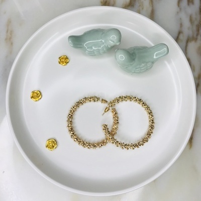 Brincos dourados, pendentes florais dourados e figuras de pássaros verdes num prato branco