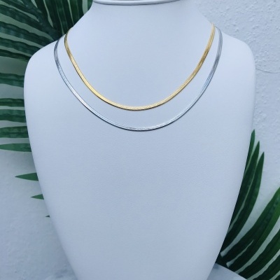 Colares dourado e prateado em suporte branco com fundo de folhas verdes