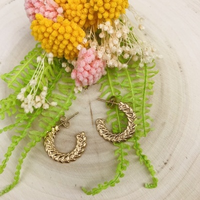 brincos dourados em argola com textura trançada em fundo de madeira com flores artificiais