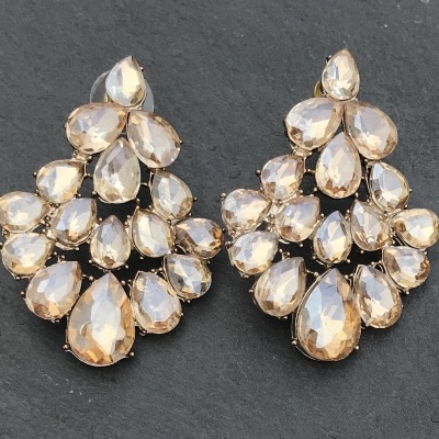 Brincos com pedras brilhantes bege e dourado em fundo preto