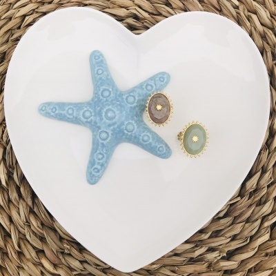 Prato branco em forma de coração com estrela-do-mar azul e dois anéis coloridos sobre tapete de palha