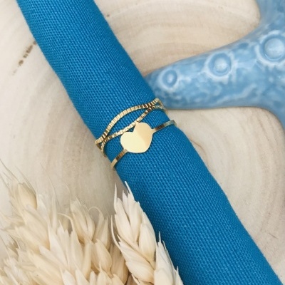 Anel dourado com coração em pano azul sobre base de madeira com trigo seco e estrela do mar