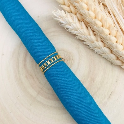 Argola dourada com corrente num guardanapo azul junto a espigas de trigo
