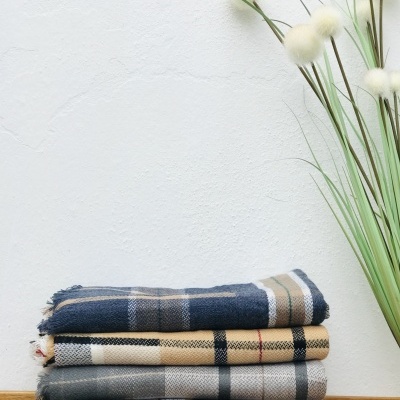 Quatro mantas ou lenços xadrez empilhados sobre superfície de madeira com ramos decorativos