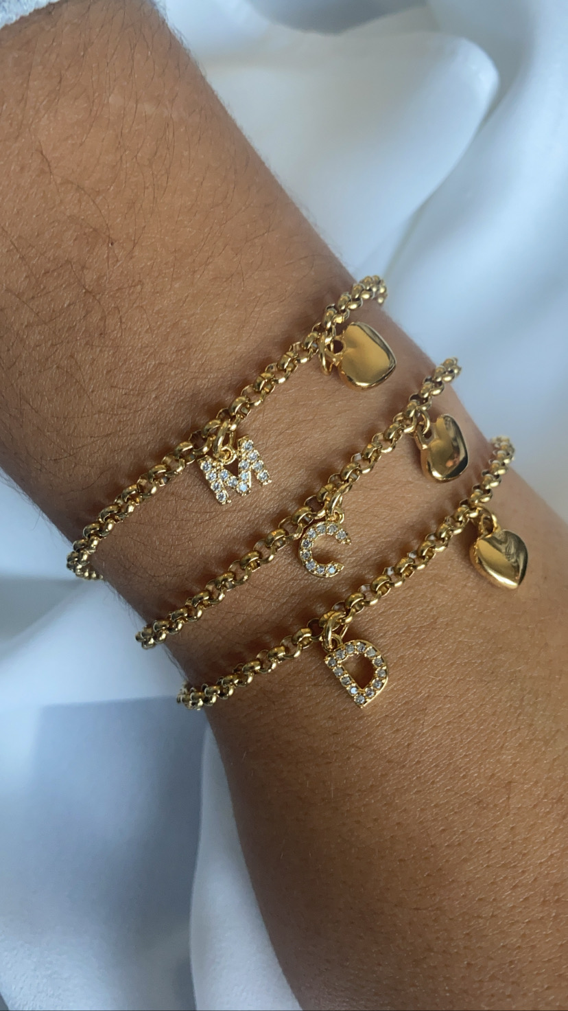 Três pulseiras douradas com letras e corações