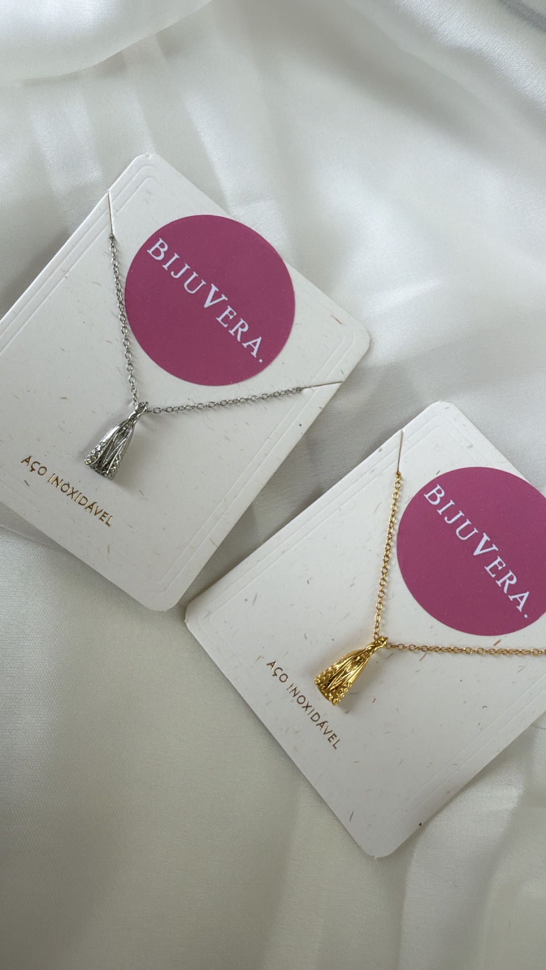Colares BIJUVERA prateado e dourado em cartas brancas com círculo rosa sobre tecido branco