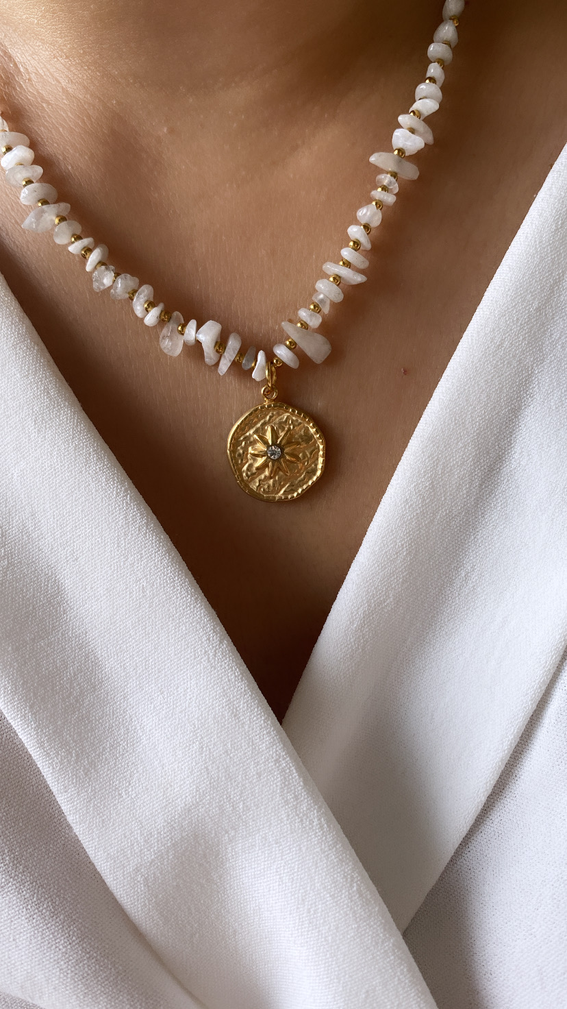 Colar com contas brancas e pendente dourado redondo sobre camisa branca