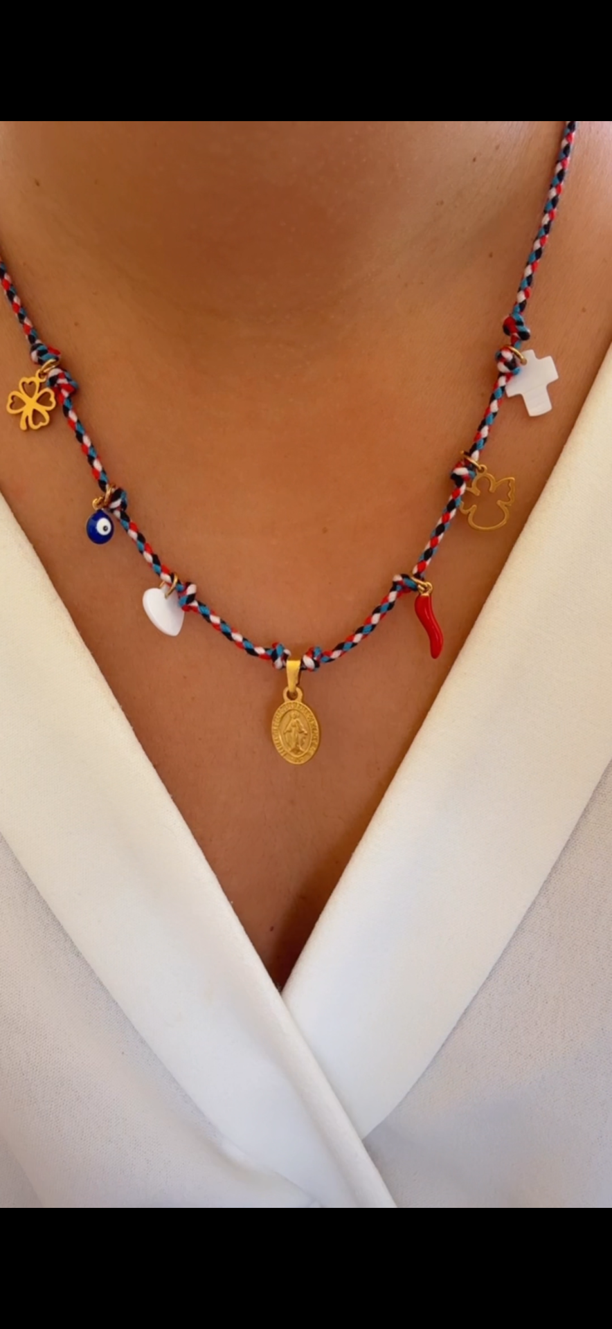 Colar colorido com diversos pendentes sobre roupa branca.