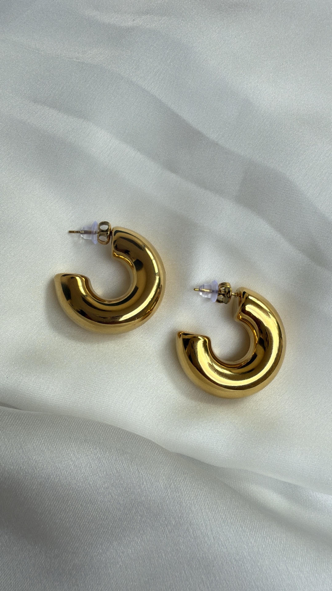 Par de brincos dourados de argola sobre tecido branco