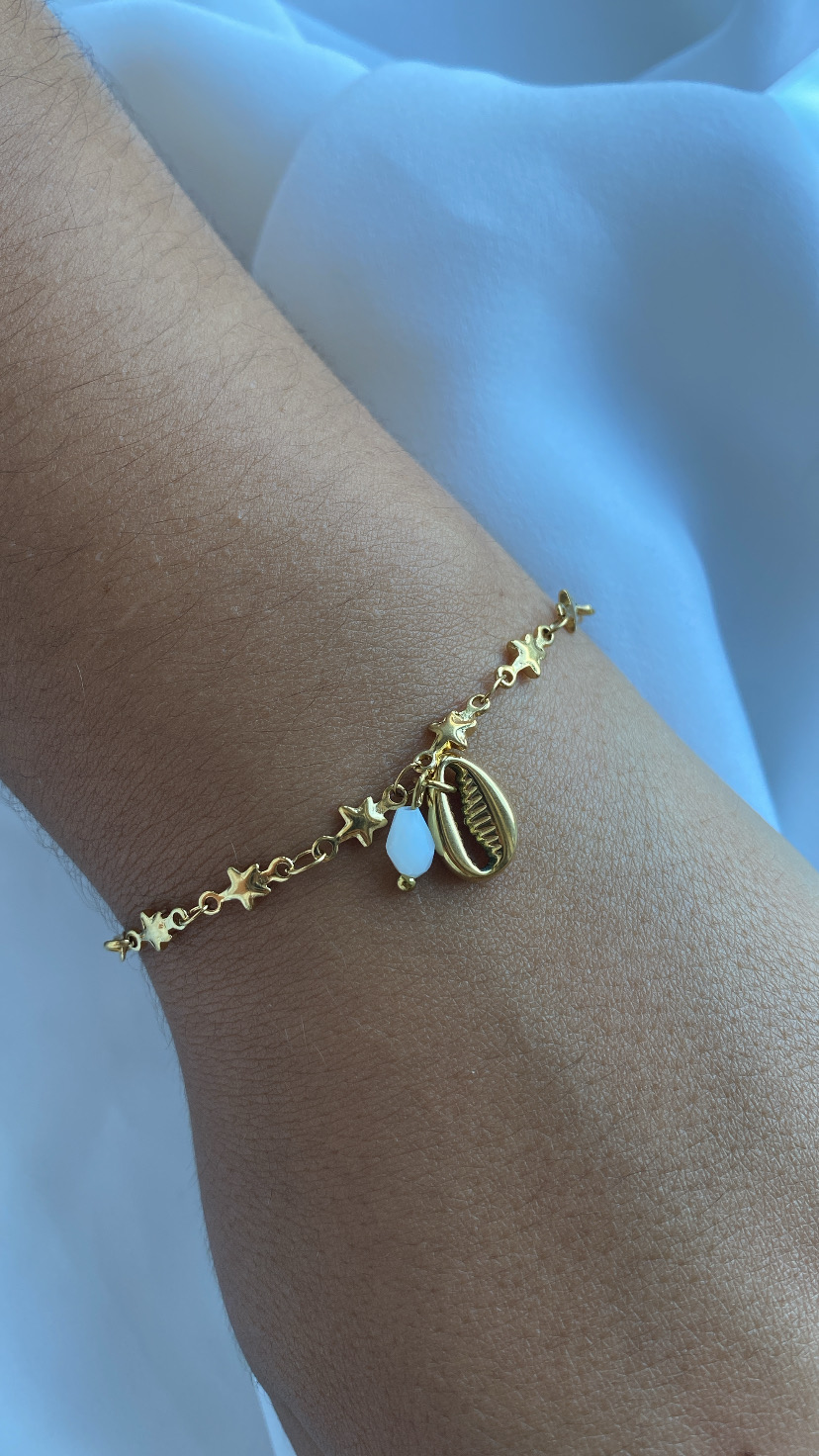 Pulseira dourada com estrelas e pendentes no pulso