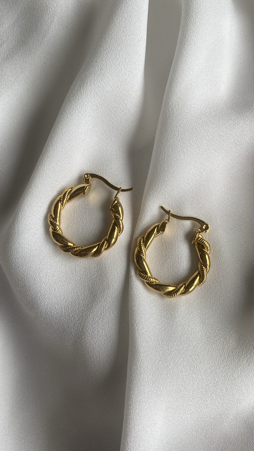 Brincos de argola dourados torcidos sobre tecido branco