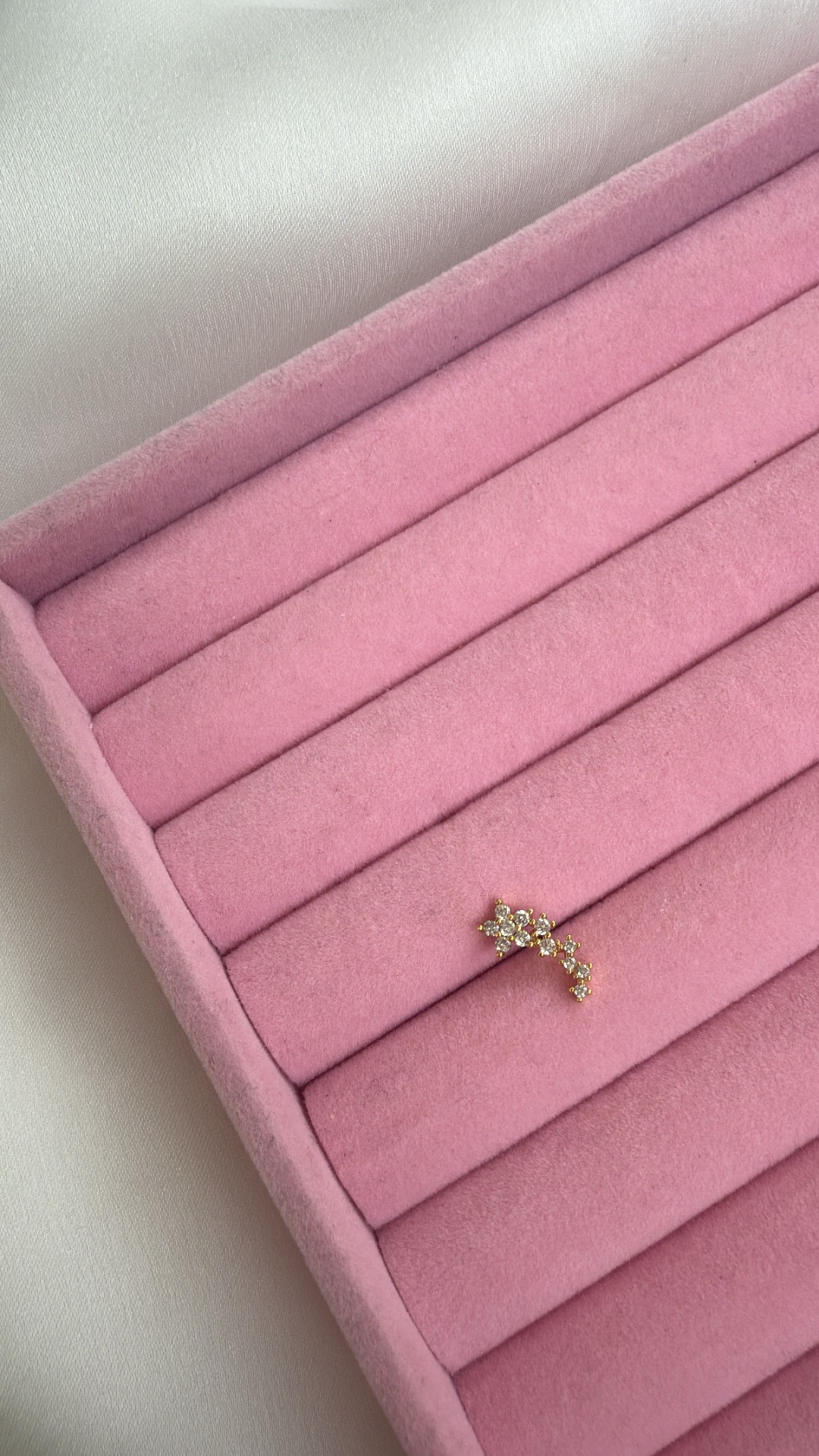 Brinco dourado com cristais numa bandeja rosa almofadada