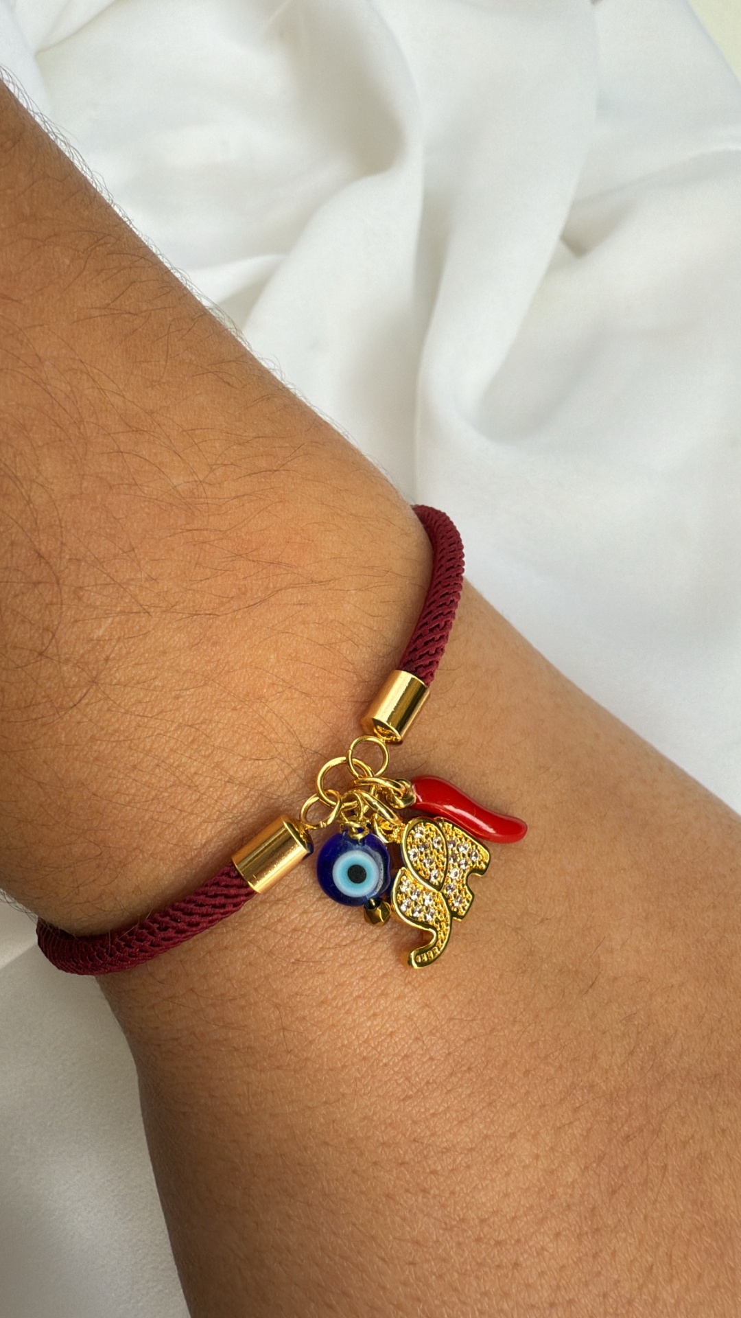 Pulseira vermelha com pendentes dourados, olho azul e corno vermelho no pulso