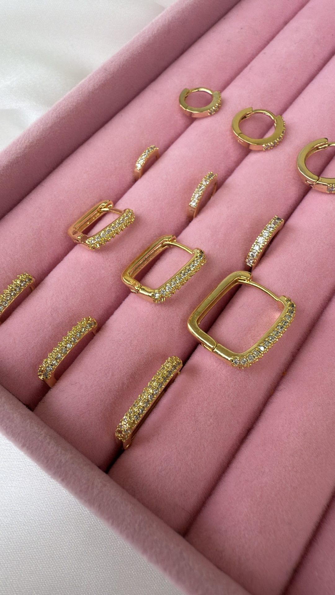 Conjunto de brincos dourados com pedras brilhantes em estojo rosa de veludo