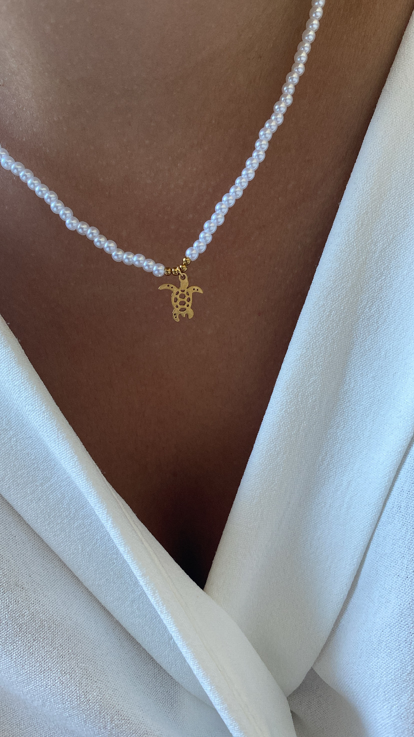 Colar de pérolas com pendente de tartaruga dourado sobre pele e roupa branca