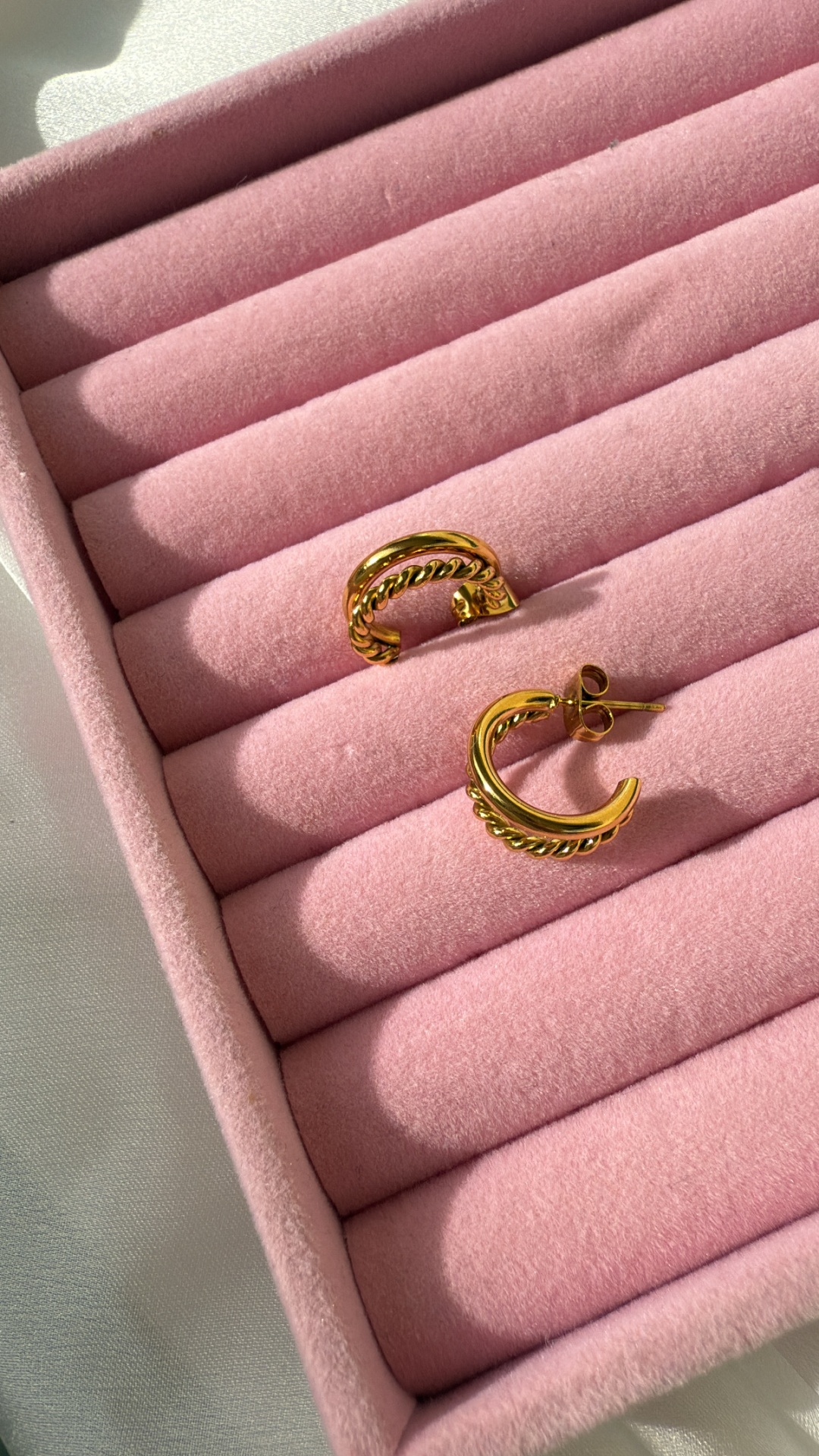 Par de brincos dourados com design de correntes numa caixa rosa acolchoada