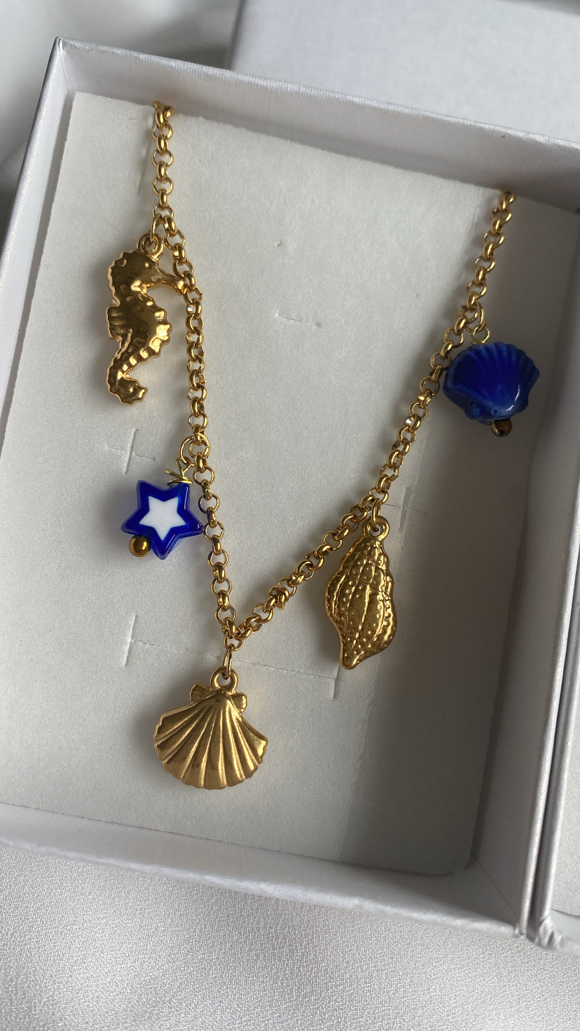 Colar dourado com pendentes marinhos numa caixa branca