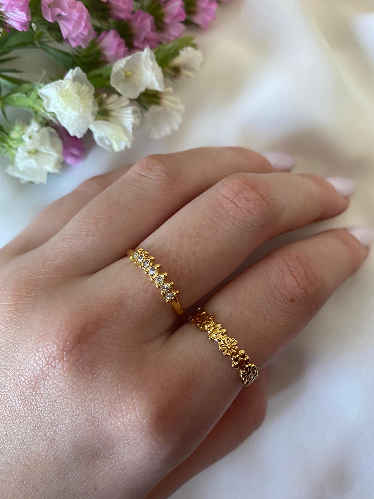 Duas alianças douradas em dedo com flores ao fundo