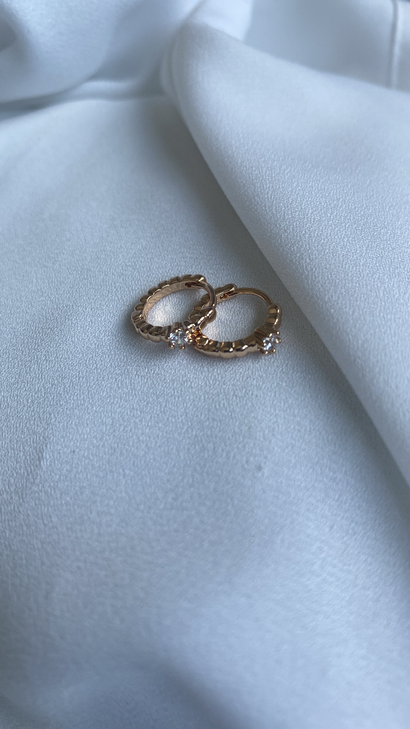 Brincos pequenos de argola dourados com pedras sobre tecido branco