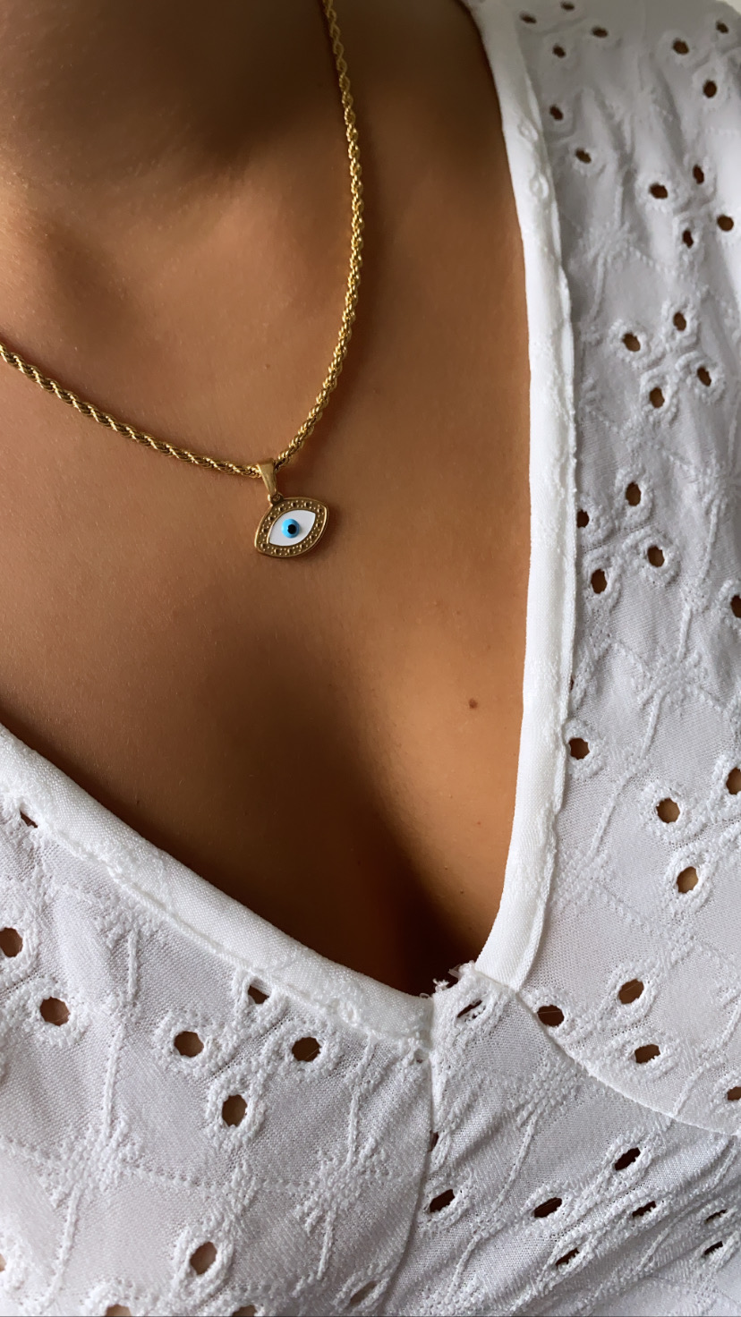 Colar dourado com pendente olho azul sobre blusa branca bordada
