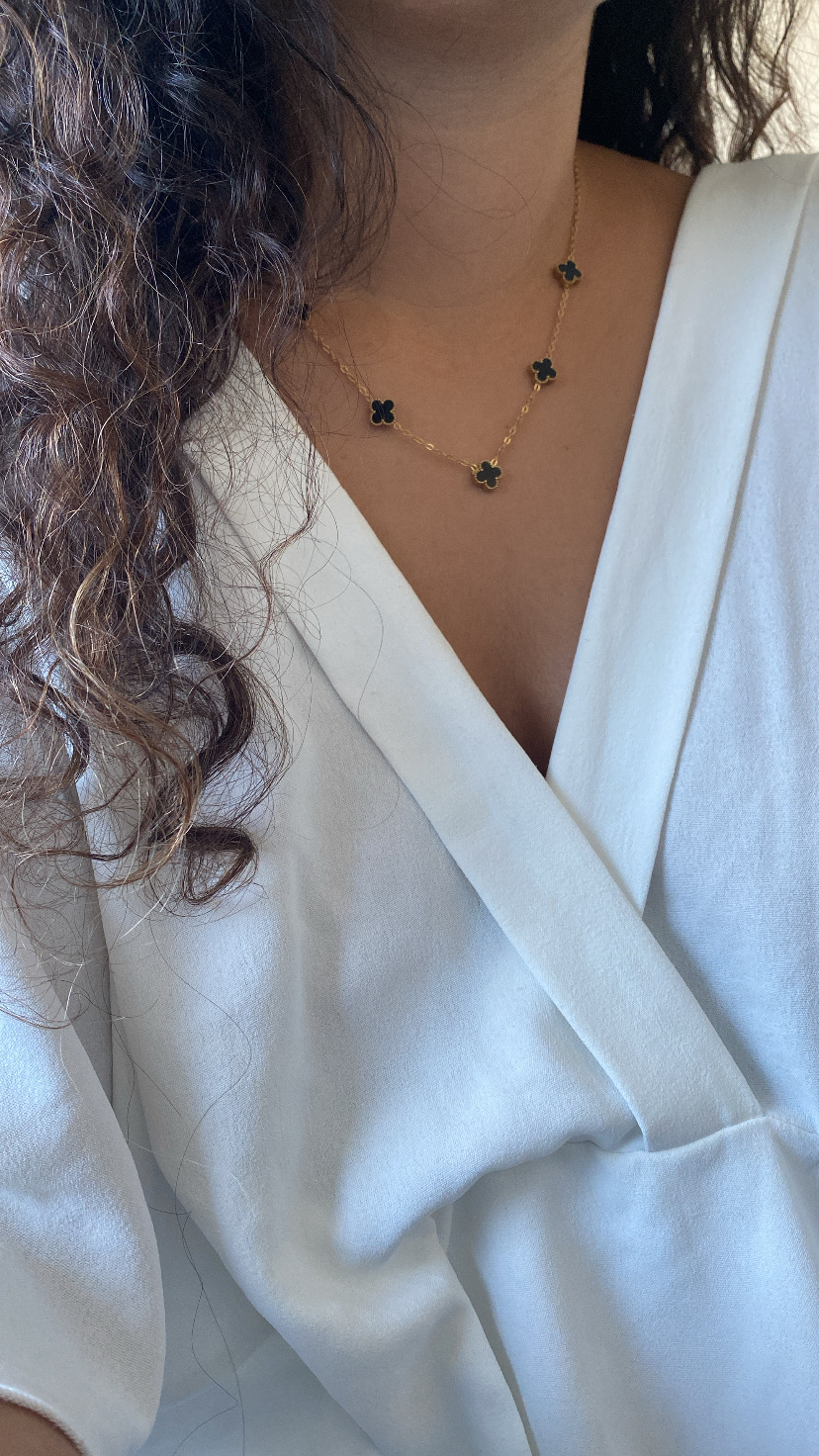 Colar dourado com flores pretas em pescoço com blusa branca