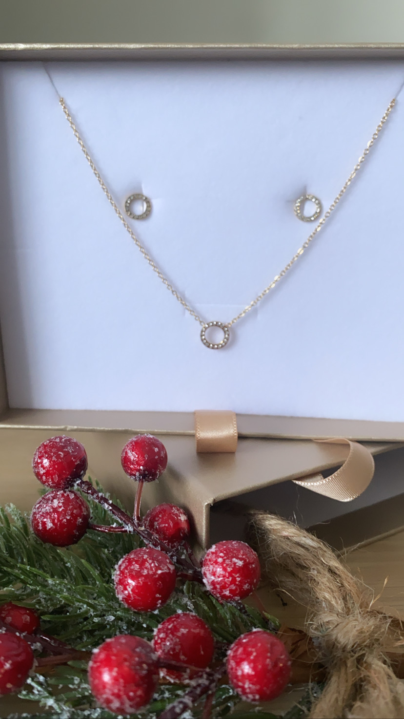 Conjunto de joias douradas com colar e brincos numa caixa de presente dourada decorada com bagas vermelhas.
