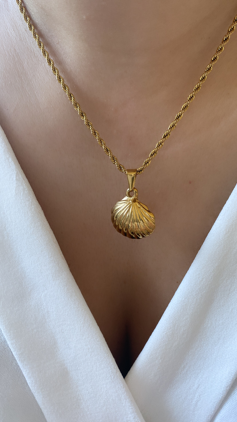 Colar dourado com pingente de concha usado no pescoço