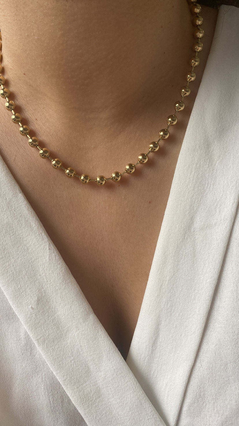 Colar dourado com contas redondas usado com camisa branca