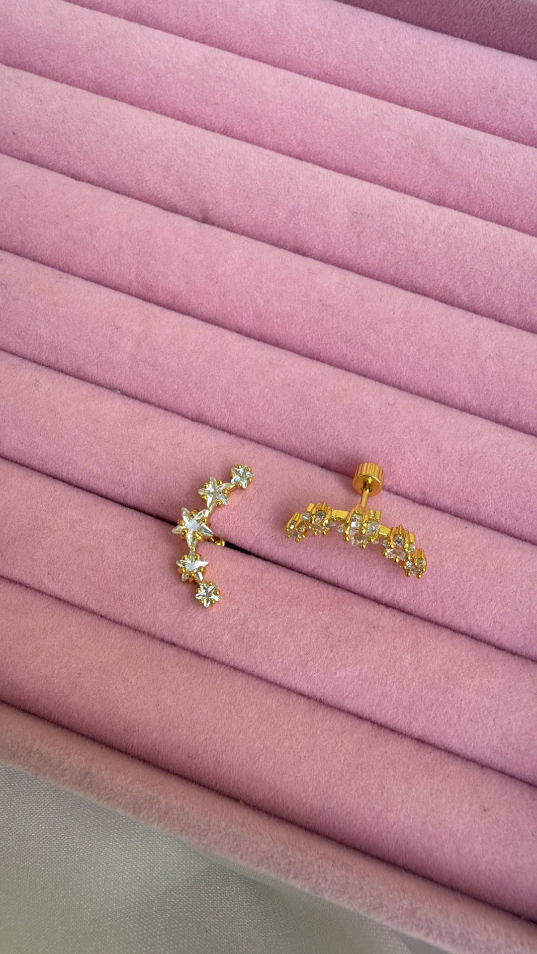 Brincos dourados com pedras em superfície almofadada rosa