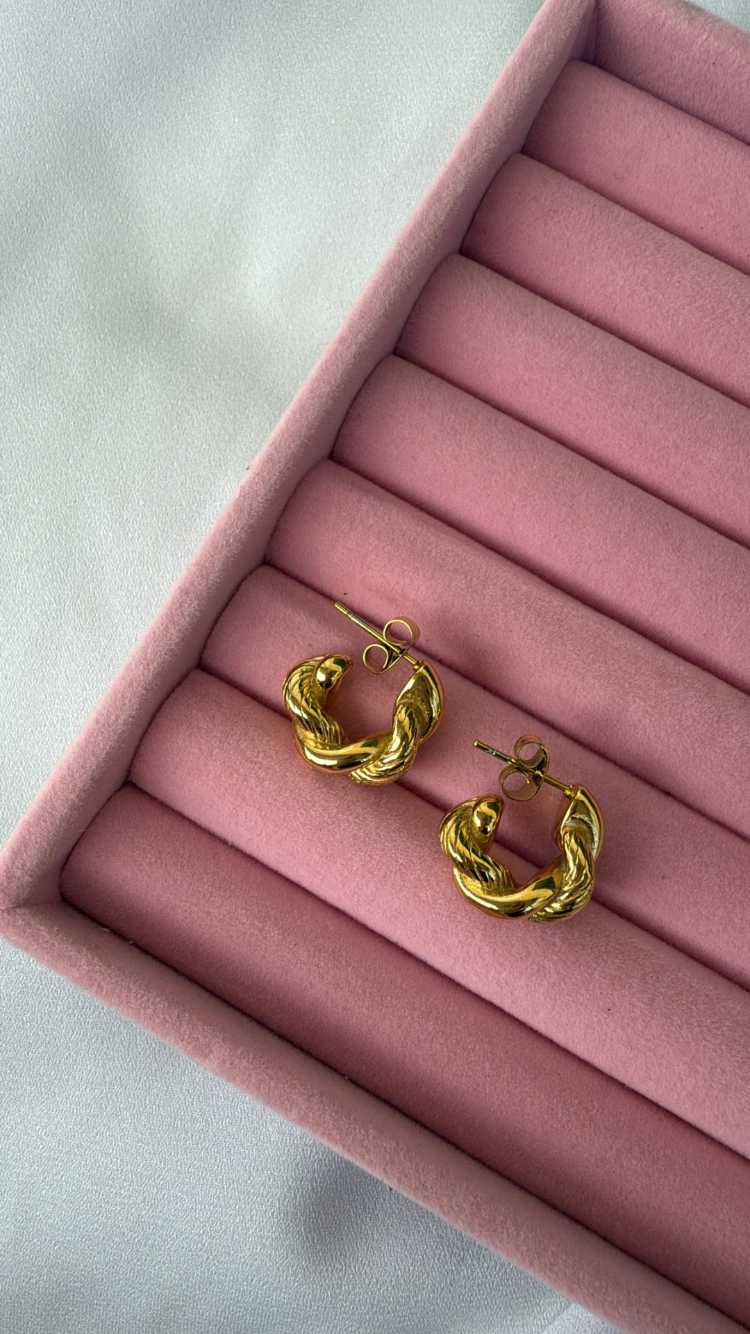 Brincos dourados torcidos em suporte cor de rosa