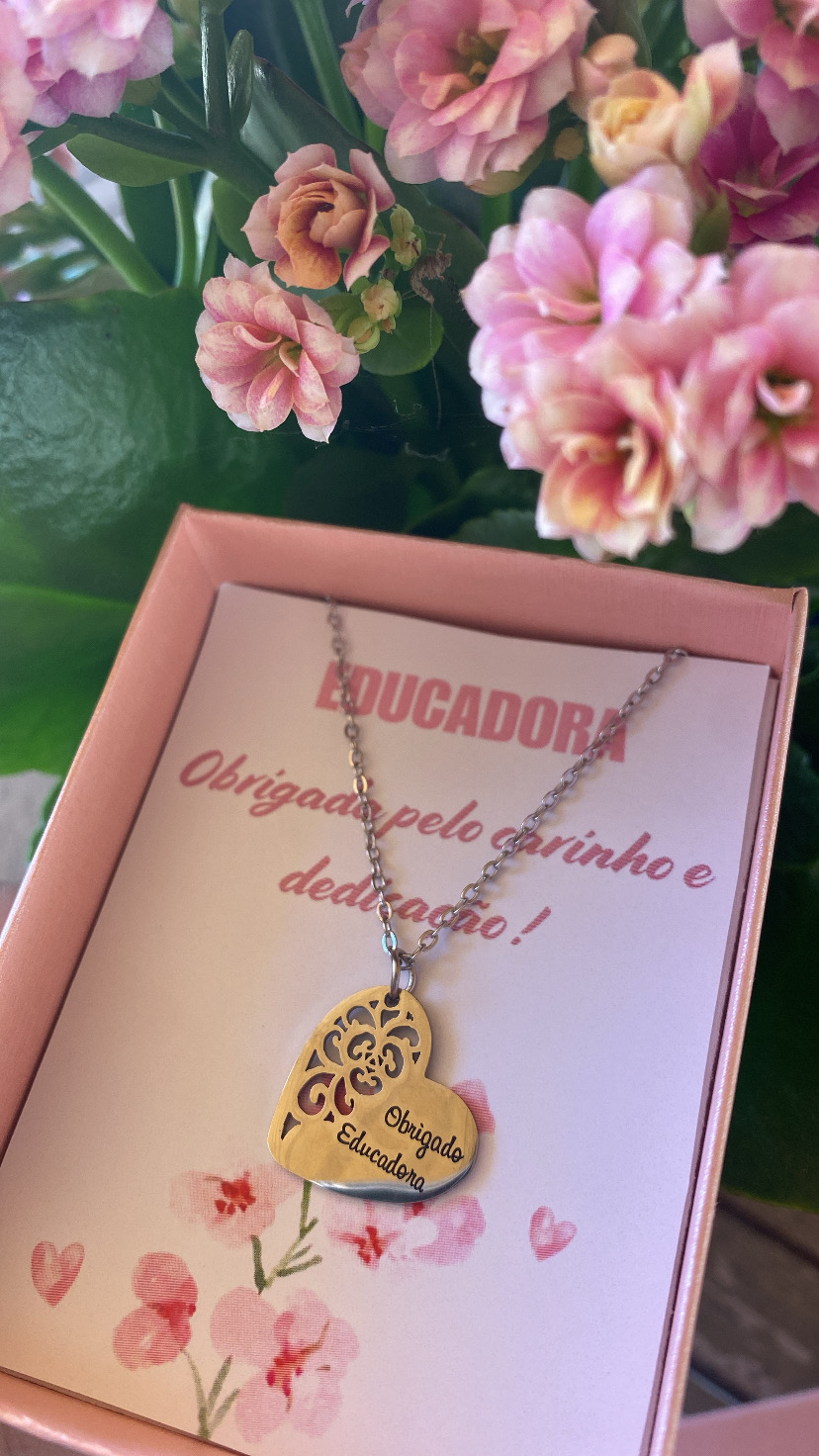 Colar com pingente em forma de coração dourado para educadora com caixa rosa e flores ao fundo