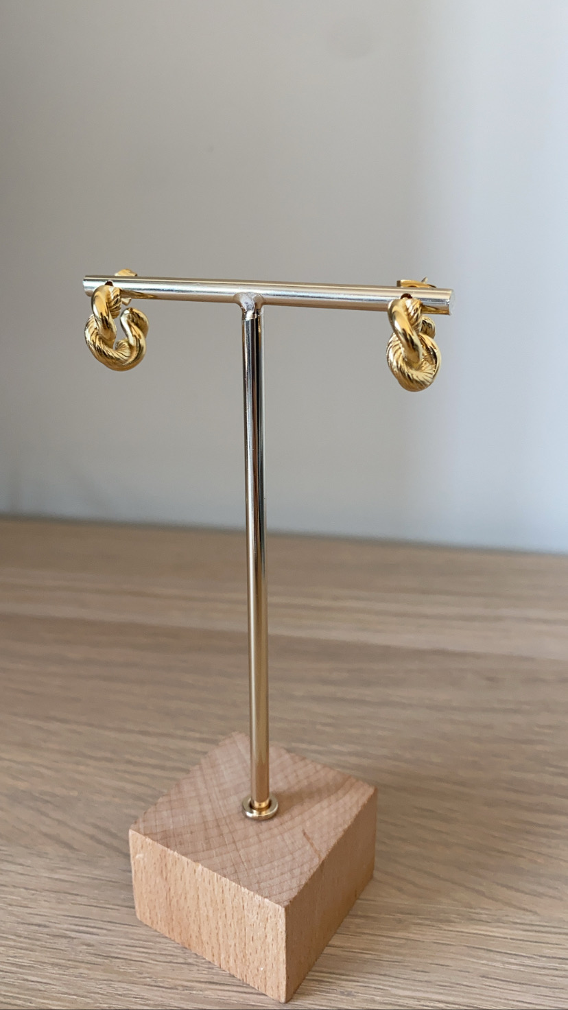 Brincos dourados entrelaçados em suporte metálico prateado com base de madeira