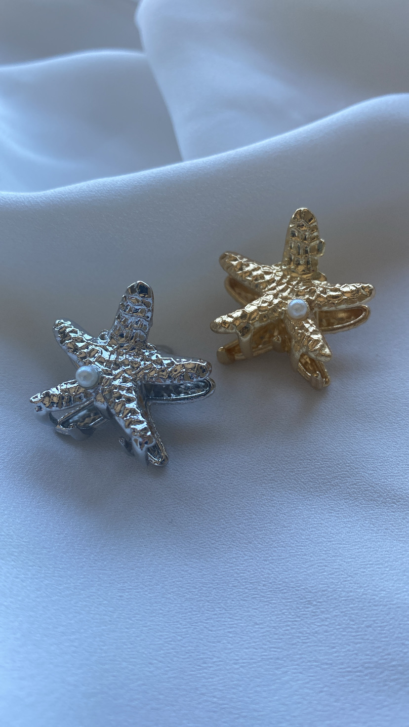 clips de cabelo em forma de estrela-do-mar prateado e dourado com pérola no centro sobre tecido branco