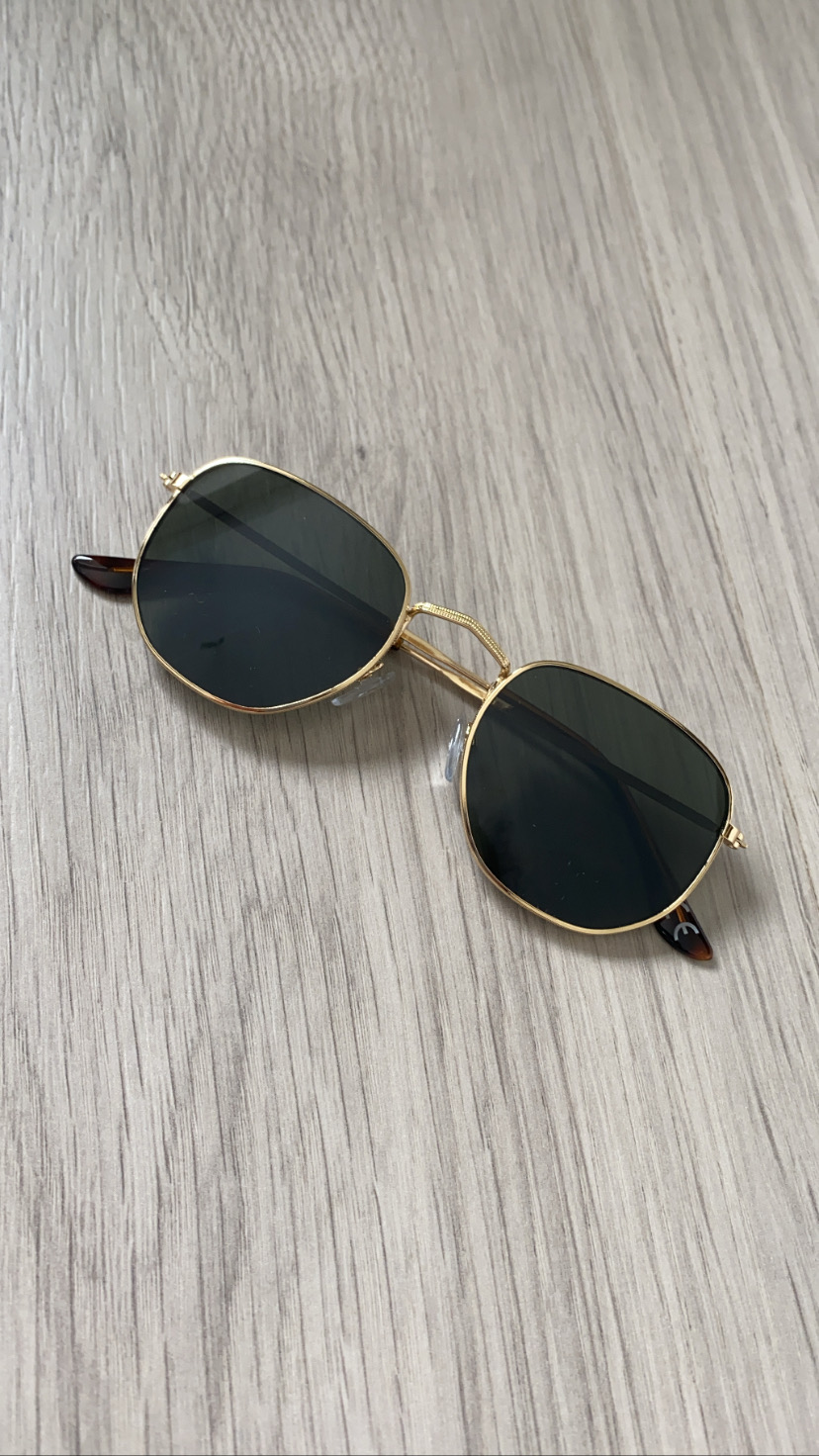 Óculos de sol dourados com lentes escuras sobre madeira clara