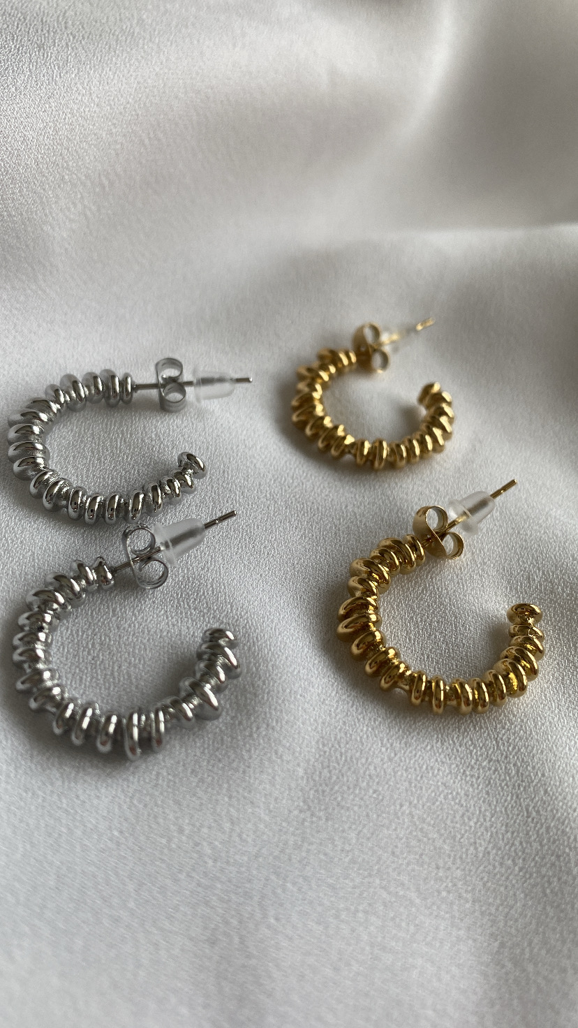 Dois pares de brincos argola, prateado e dourado, textura espiral metálica sobre tecido branco