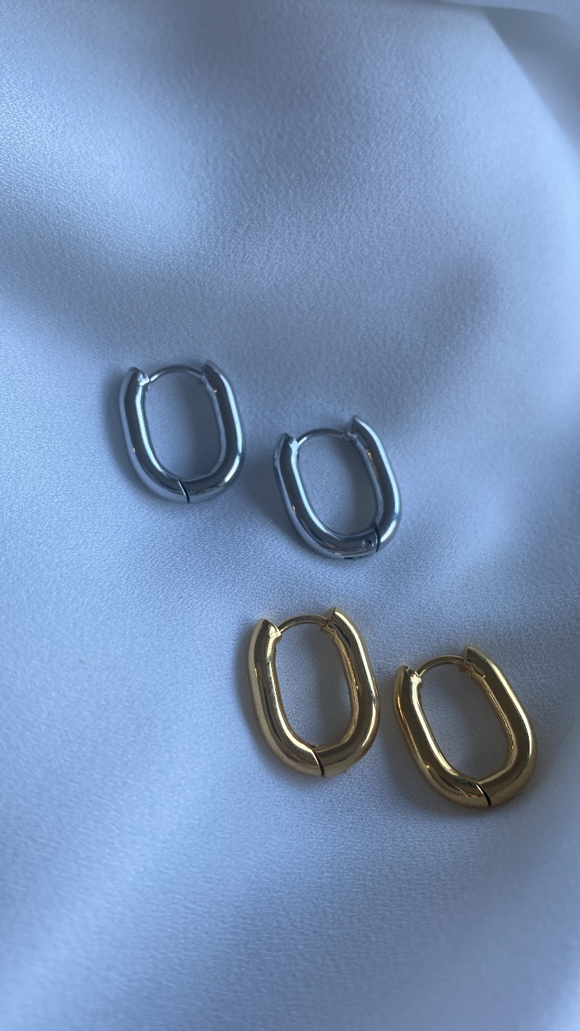 Dois pares de brincos argola oval em metal prateado e dourado sobre tecido branco