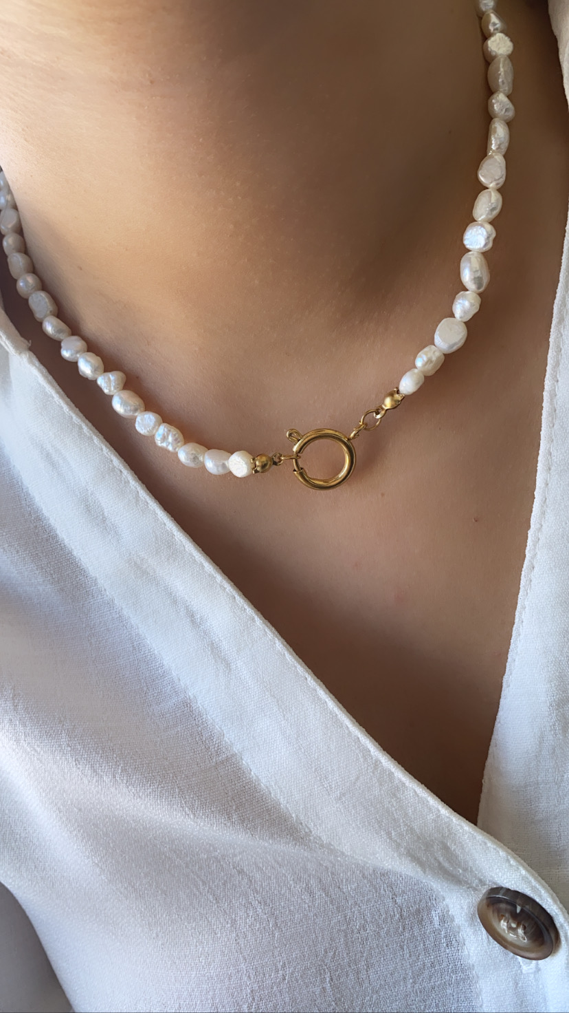 Colar de pérolas com fecho dourado sobre blusa branca