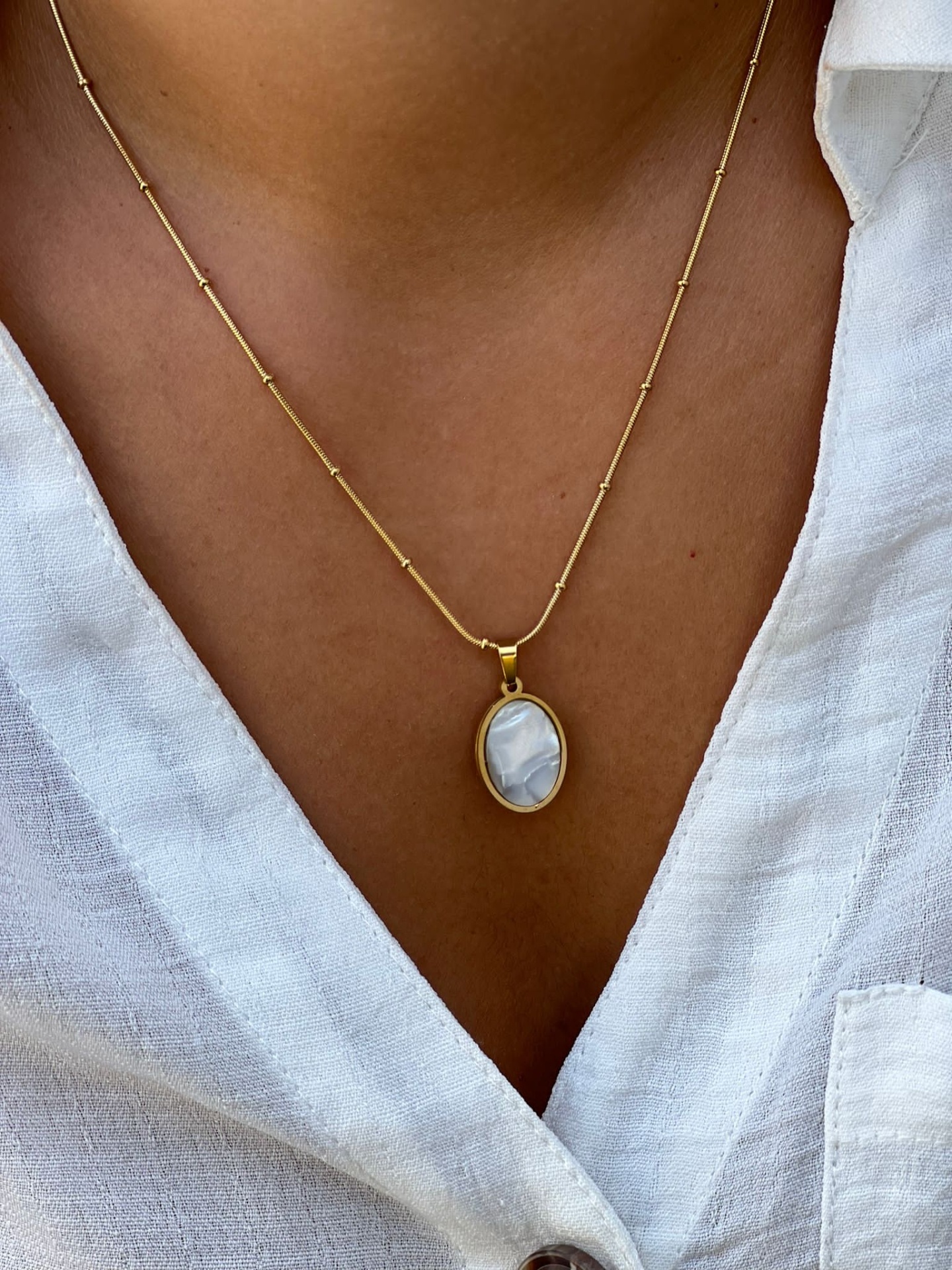 Colar dourado com pendente oval azul claro sobre camisa branca