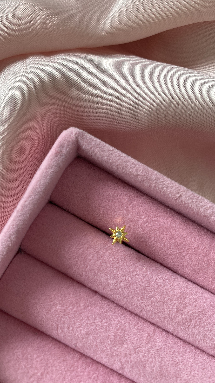 Anel estrela dourado com pedra num suporte rosa de veludo