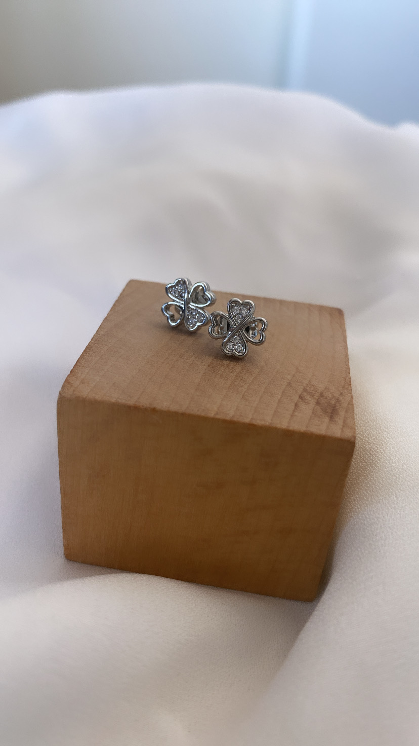 Brincos prateados em forma de trevo com pedras, sobre cubo de madeira
