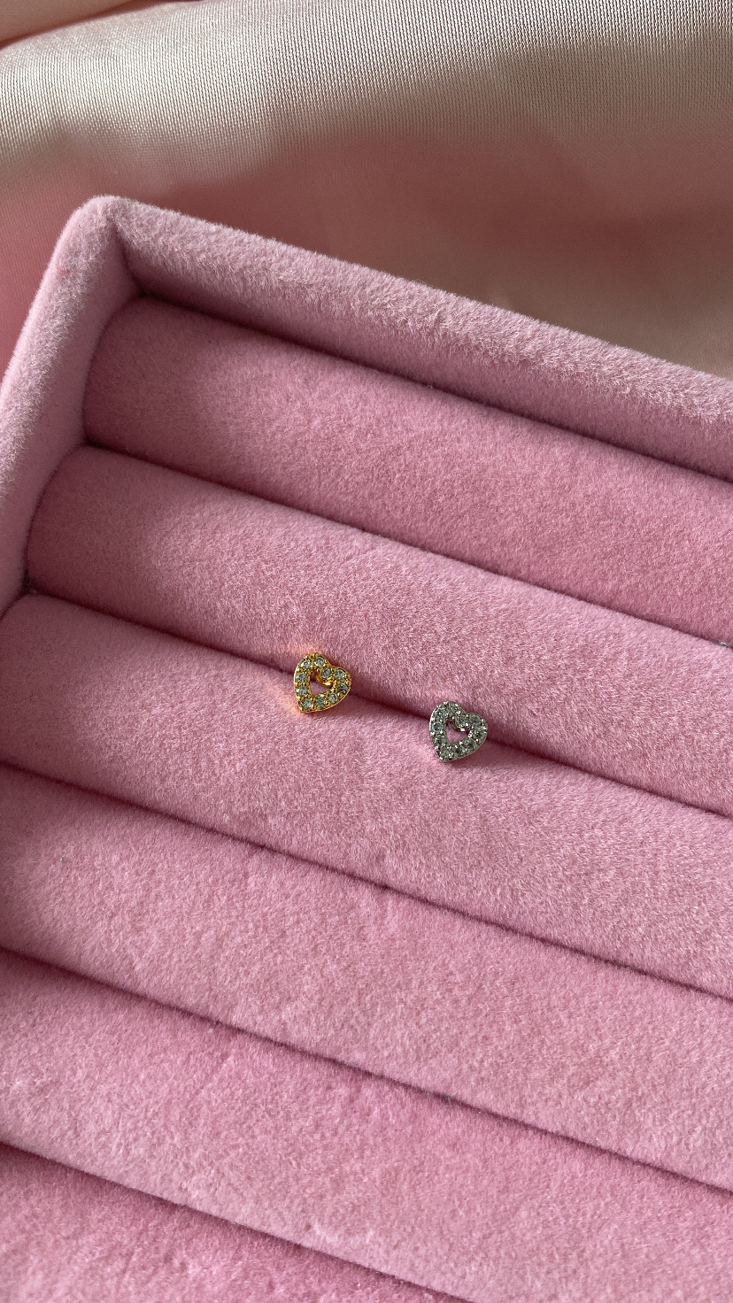 Brincos de coração dourado e prateado com pedras, sobre caixa rosa acolchoada