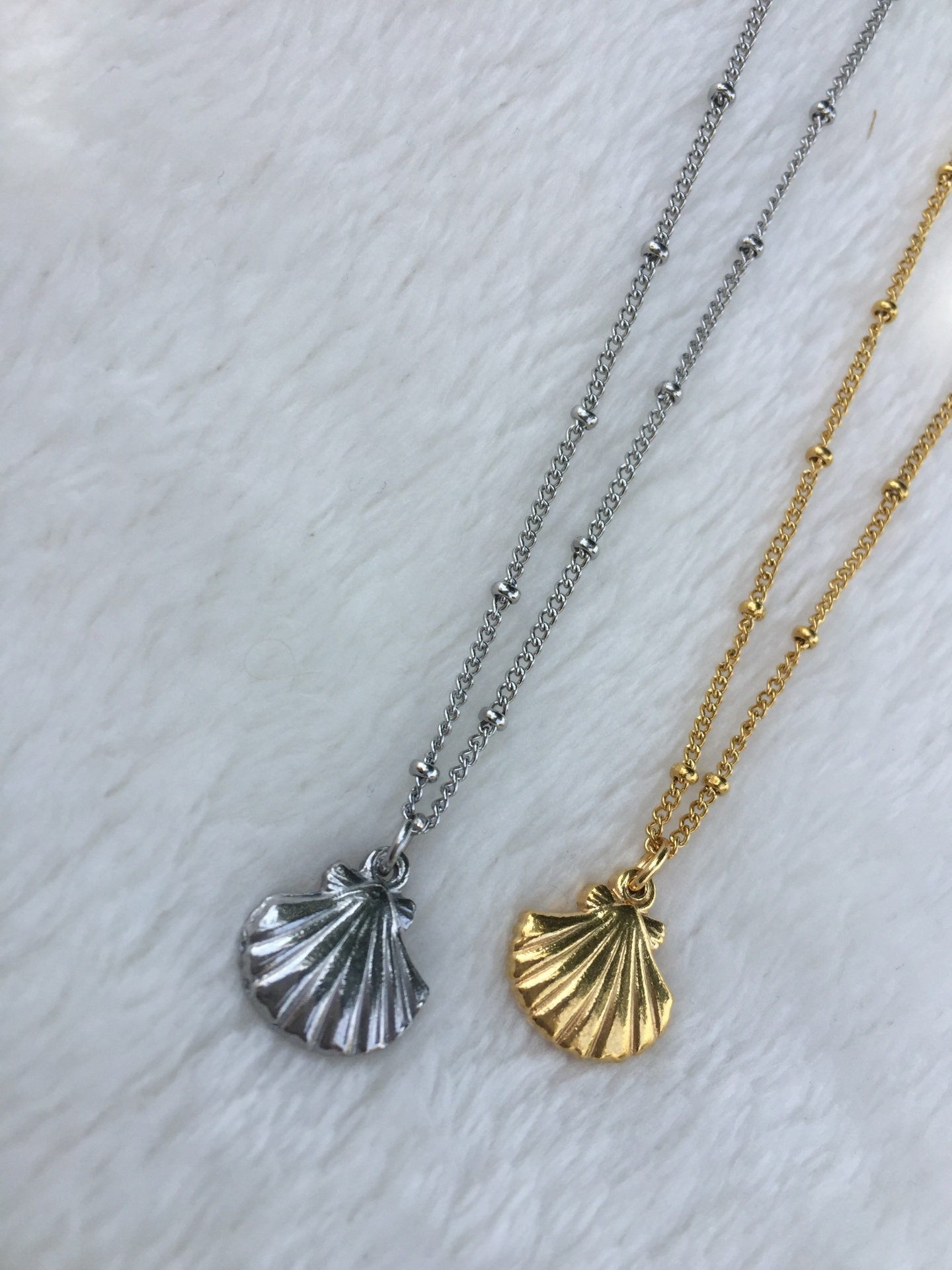 Colares com pendentes de concha em prata e dourado sobre superfície branca felpuda