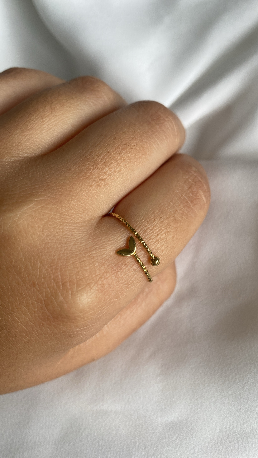 Anel dourado com coração e esfera numa mão sobre tecido branco