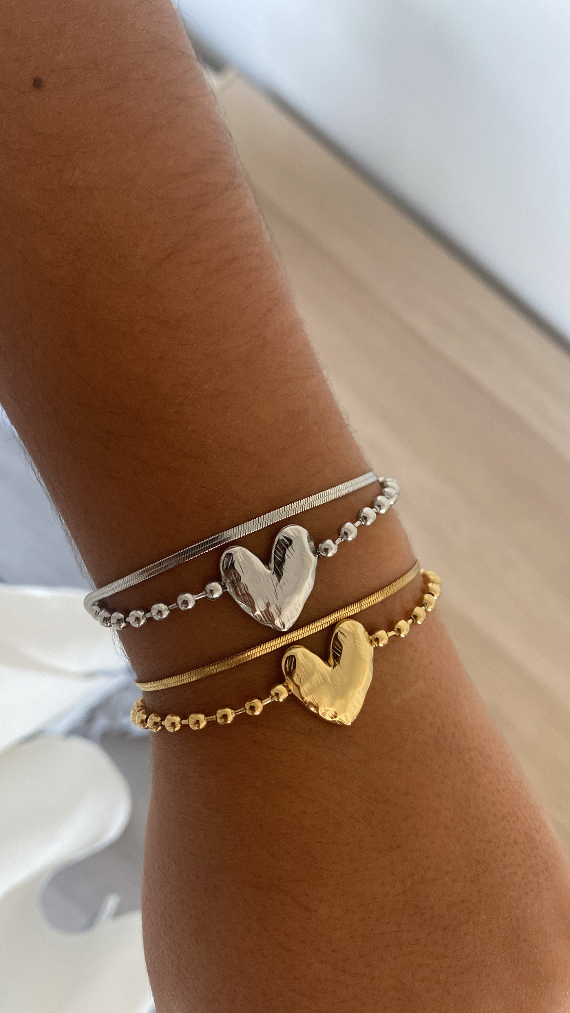 Pulseiras dourada e prateada com corações metálicos no pulso