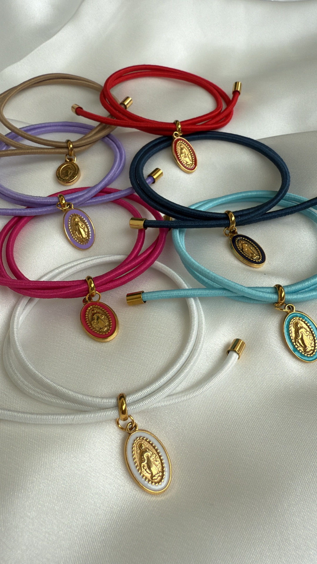 Pulseiras coloridas com pendentes ovalados dourados sobre tecido branco