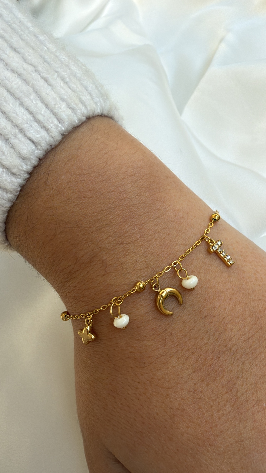 Pulseira dourada com pendentes variados no pulso