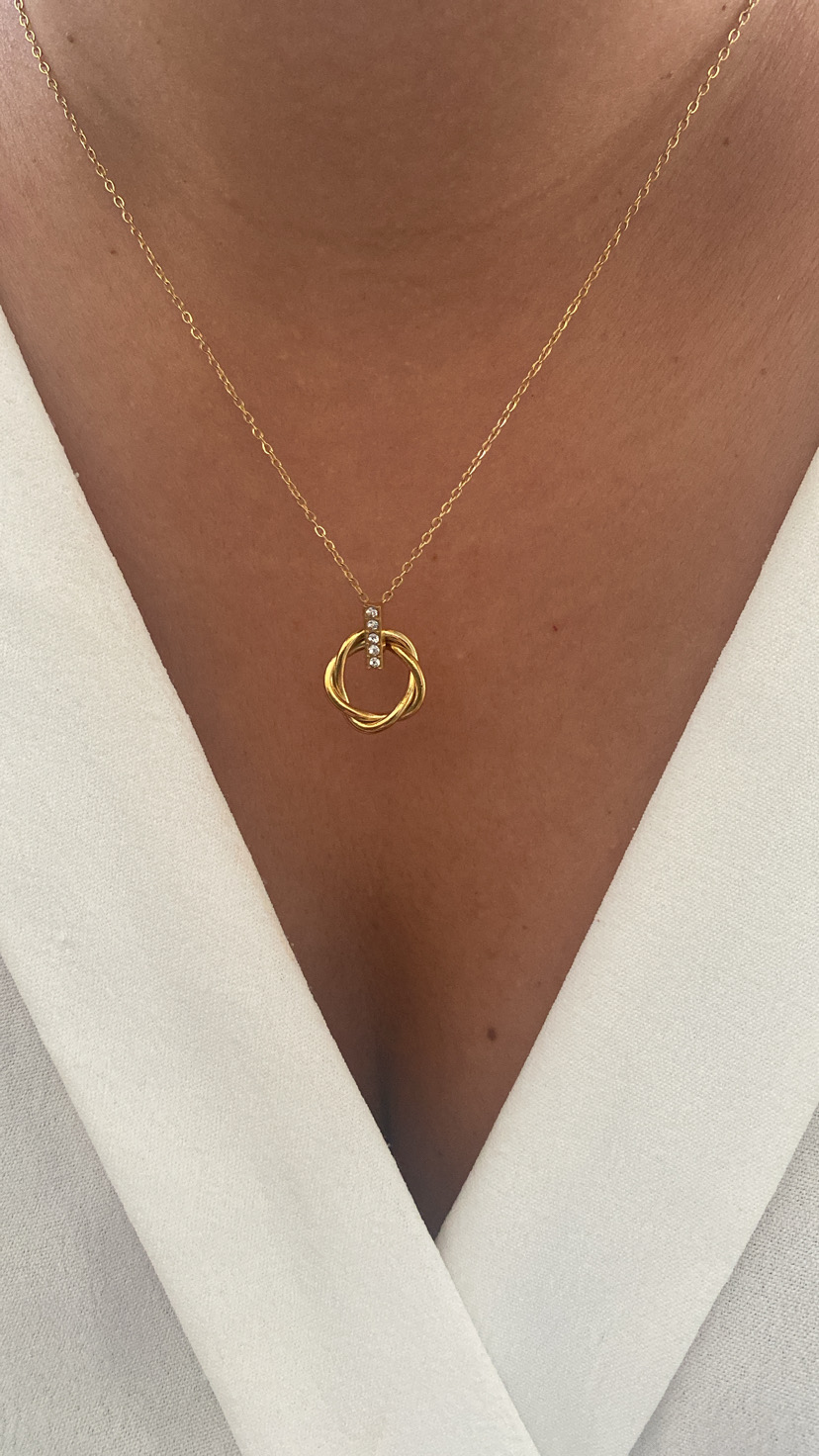 Colar dourado com três argolas entrelaçadas e brilhantes, em vestido branco decote V.